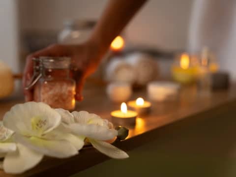 Tafel met waxinelichtjes, orchideeën en blured hand met een potje beauty producten